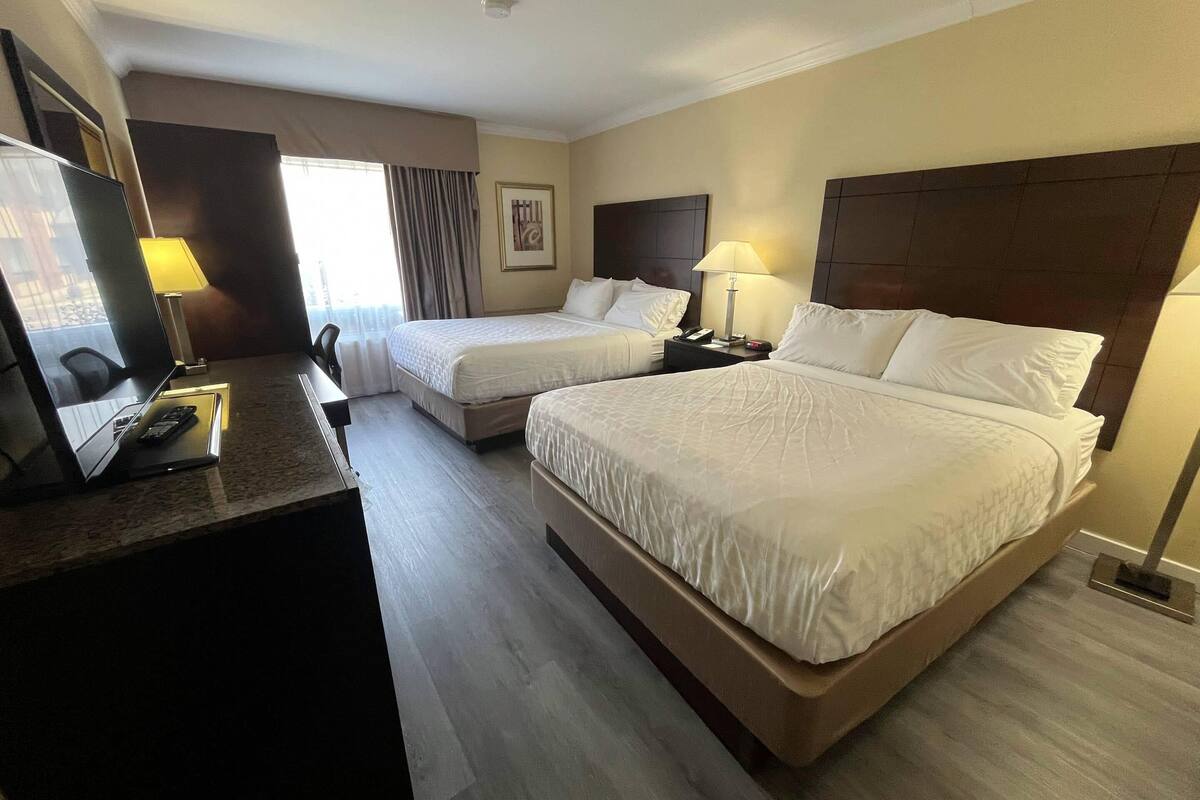 A hotel room with two beds, a desk with a computer, and a window with curtains.