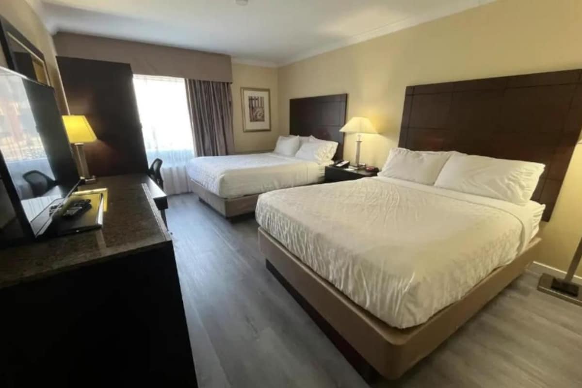 A hotel room with two beds, a desk with a lamp, and a television.
