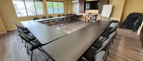 A conference room with a long table, chairs, a whiteboard, and a TV.