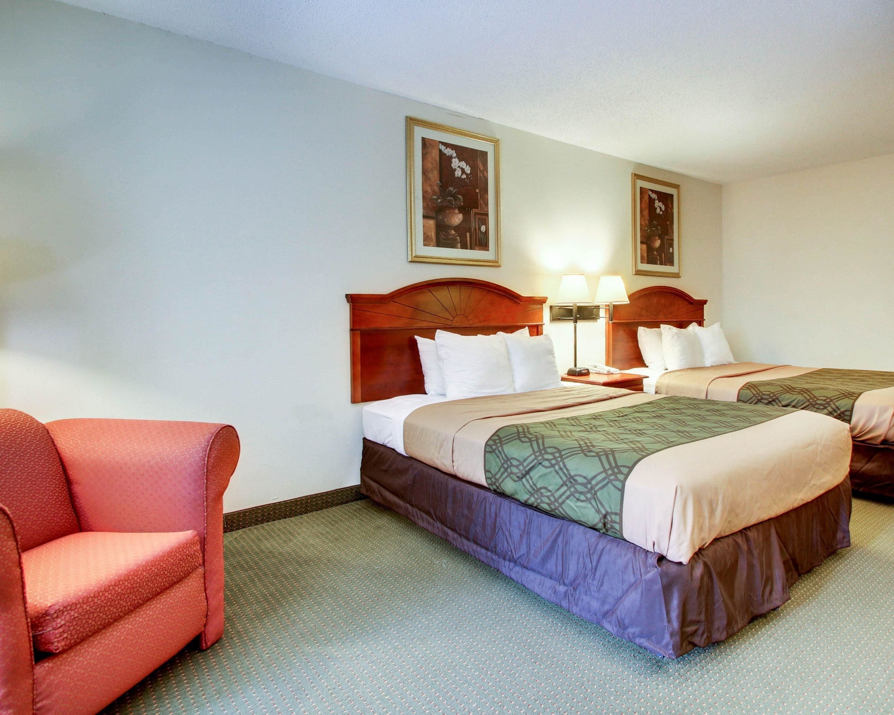 A hotel room with two beds, a chair, and two lamps.