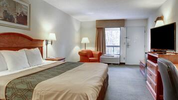 A hotel room with a large bed, a desk with a television, a chair, and a window with curtains.