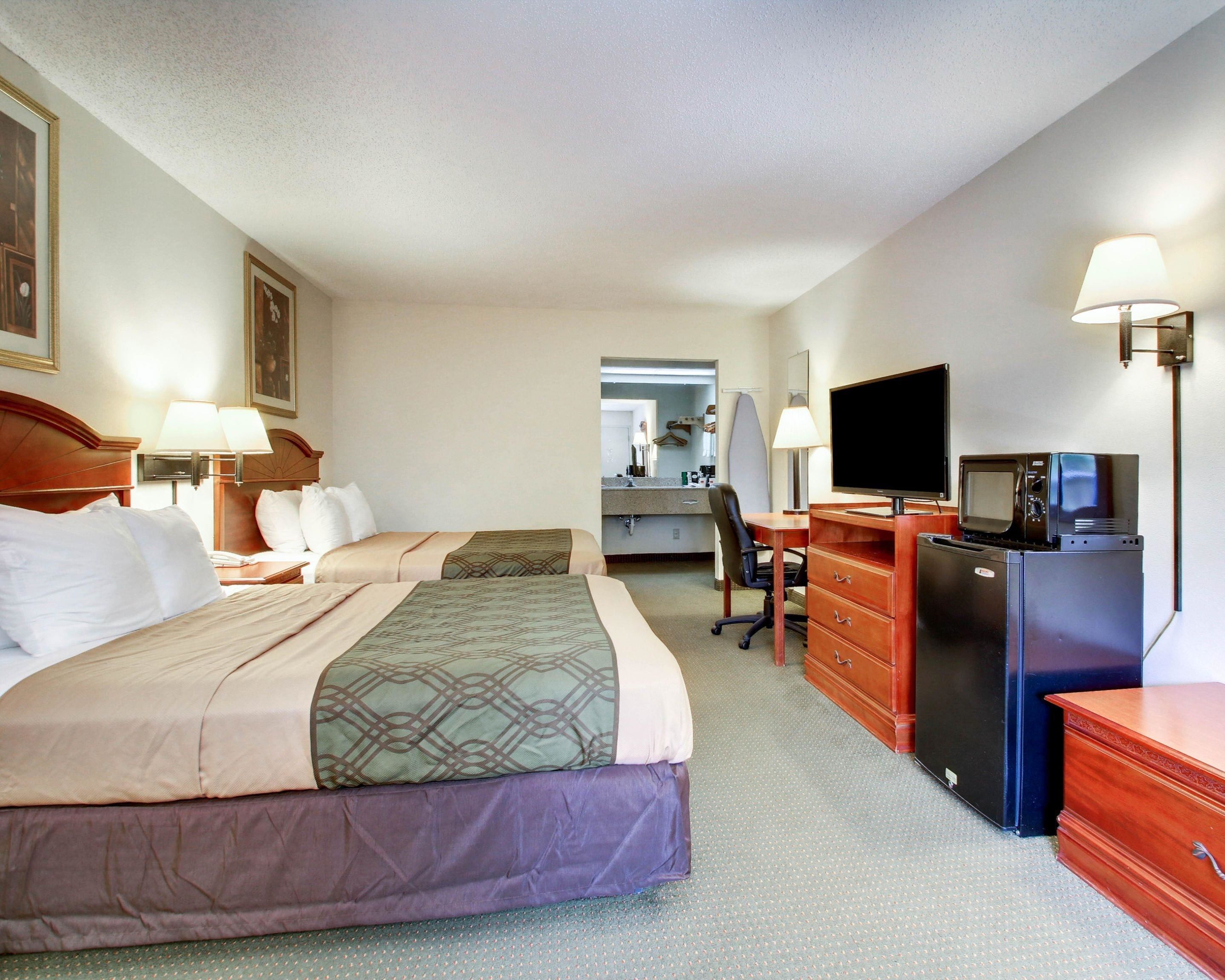 A hotel room with a large bed, a desk with a computer and a TV, a refrigerator, and a mirror.