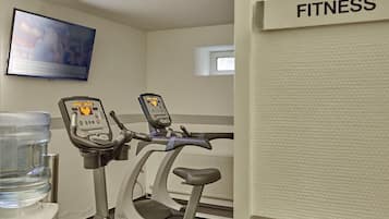 Un gimnasio con dos bicicletas estáticas, un dispensador de agua y una televisión mostrando una película.