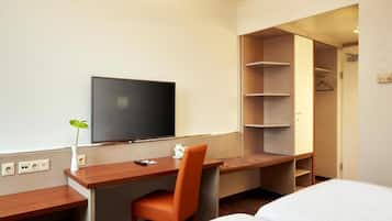 Een hotelkamer met een bed, bureau met stoel, televisie en kledingkast.