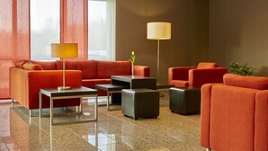 A modern lobby with orange sofas, a coffee table, and a floor lamp. - Sunday Hotel Leipzig-Halle (Landsberg)