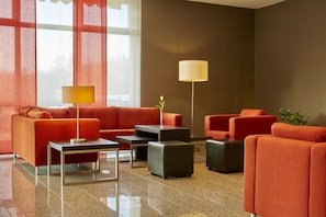 A modern lobby with orange sofas, a coffee table, and a floor lamp. - H+ Hotel Leipzig-Halle by Sunday Hotels (Landsberg)