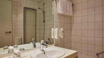 A hotel bathroom with a sink, mirror, towel rack, and shower.