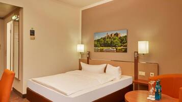 A hotel room with a bed, a desk, two chairs, and a painting on the wall.