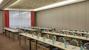 A conference room with long tables, chairs, water bottles, and a red curtain. - Sunday Hotel Leipzig-Halle (Landsberg)