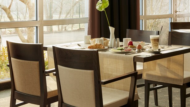 A dining table set with chairs, a vase with a plant, and various breakfast items. - Sunday Hotel Leipzig-Halle (Landsberg)