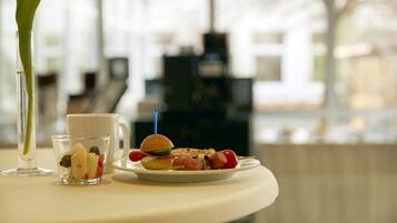 Una mesa con un vaso pequeño de fruta, una taza y un plato con una hamburguesa y verduras.