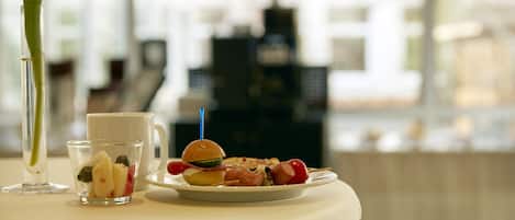A table with a small glass of fruit, a cup, and a plate with a burger and vegetables.