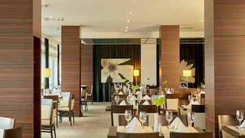 Un comedor de hotel con mesas dispuestas para los huéspedes, con un diseño moderno que incluye paneles de madera y una gran obra de arte floral en la pared.