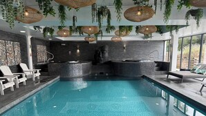 Una piscina interior con sillones de descanso, un jacuzzi y plantas colgantes.