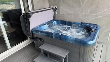 A hot tub with a bench, a covered window, and a view of greenery outside.