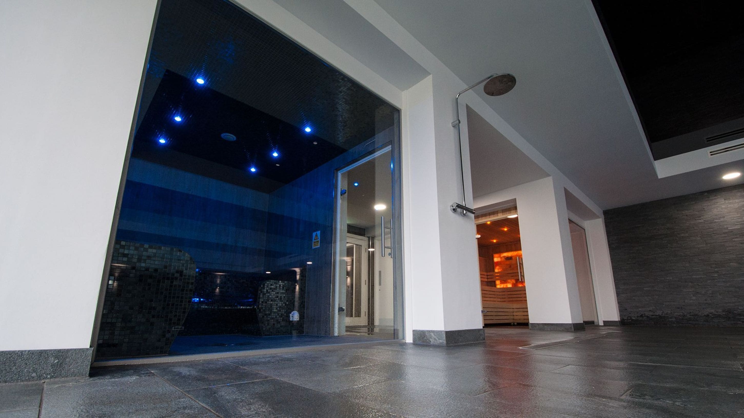 Un hall d'entrée moderne avec une façade vitrée donnant accès à un espace sauna.