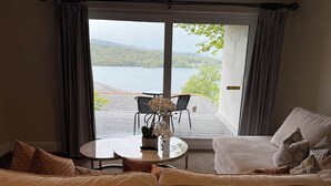 Habitación con sofá, una mesita con un florero y vistas a un lago y una terraza.