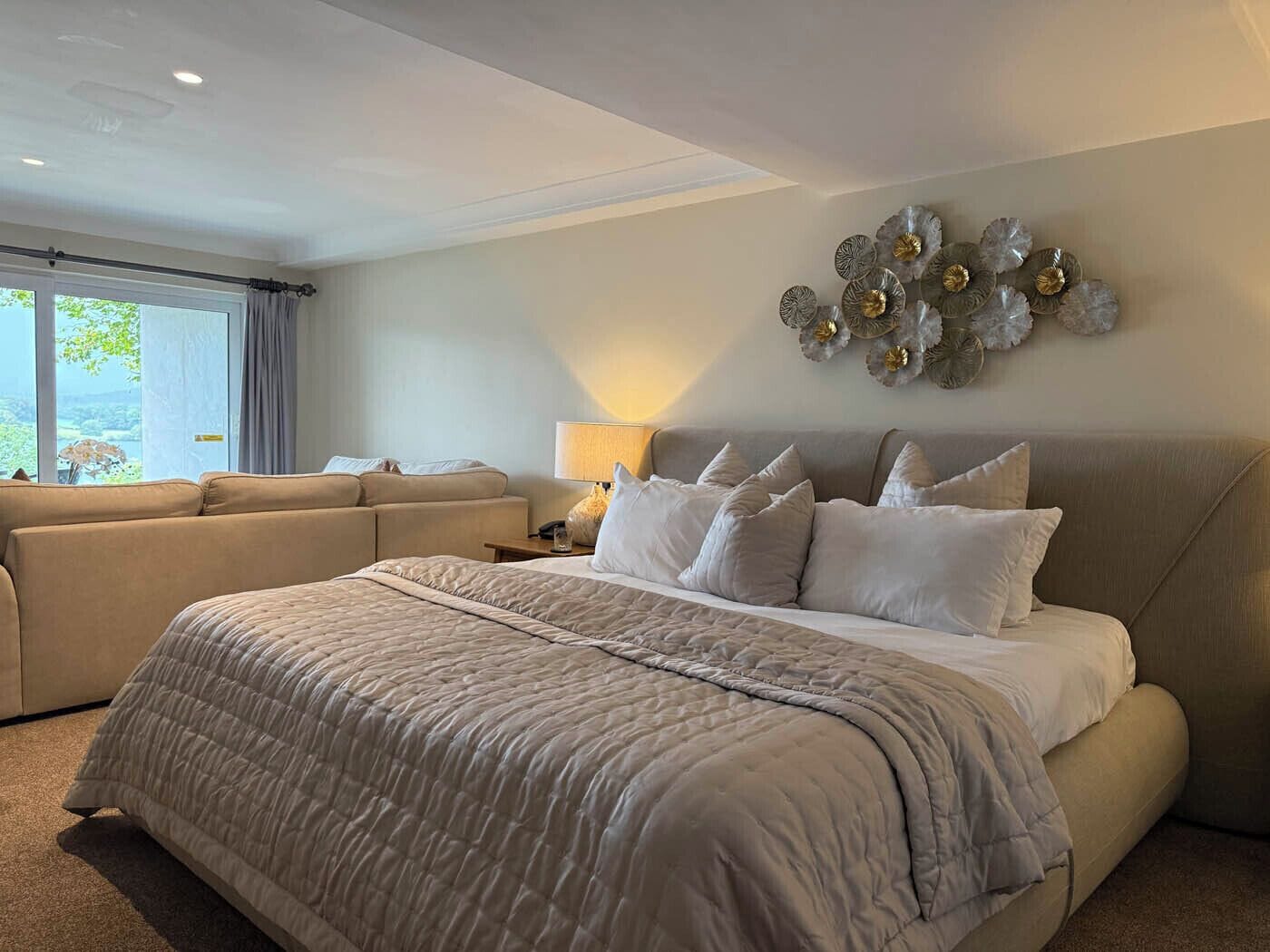 A spacious bedroom with a large bed, a sofa, and a decorative wall piece.
