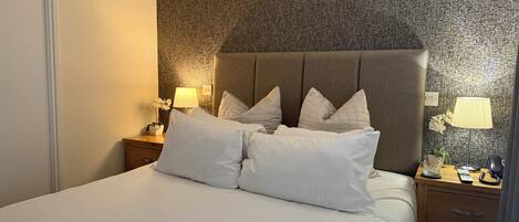 A neatly made bed with white linens and pillows, a wooden nightstand with a lamp, and a textured wall behind the bed.