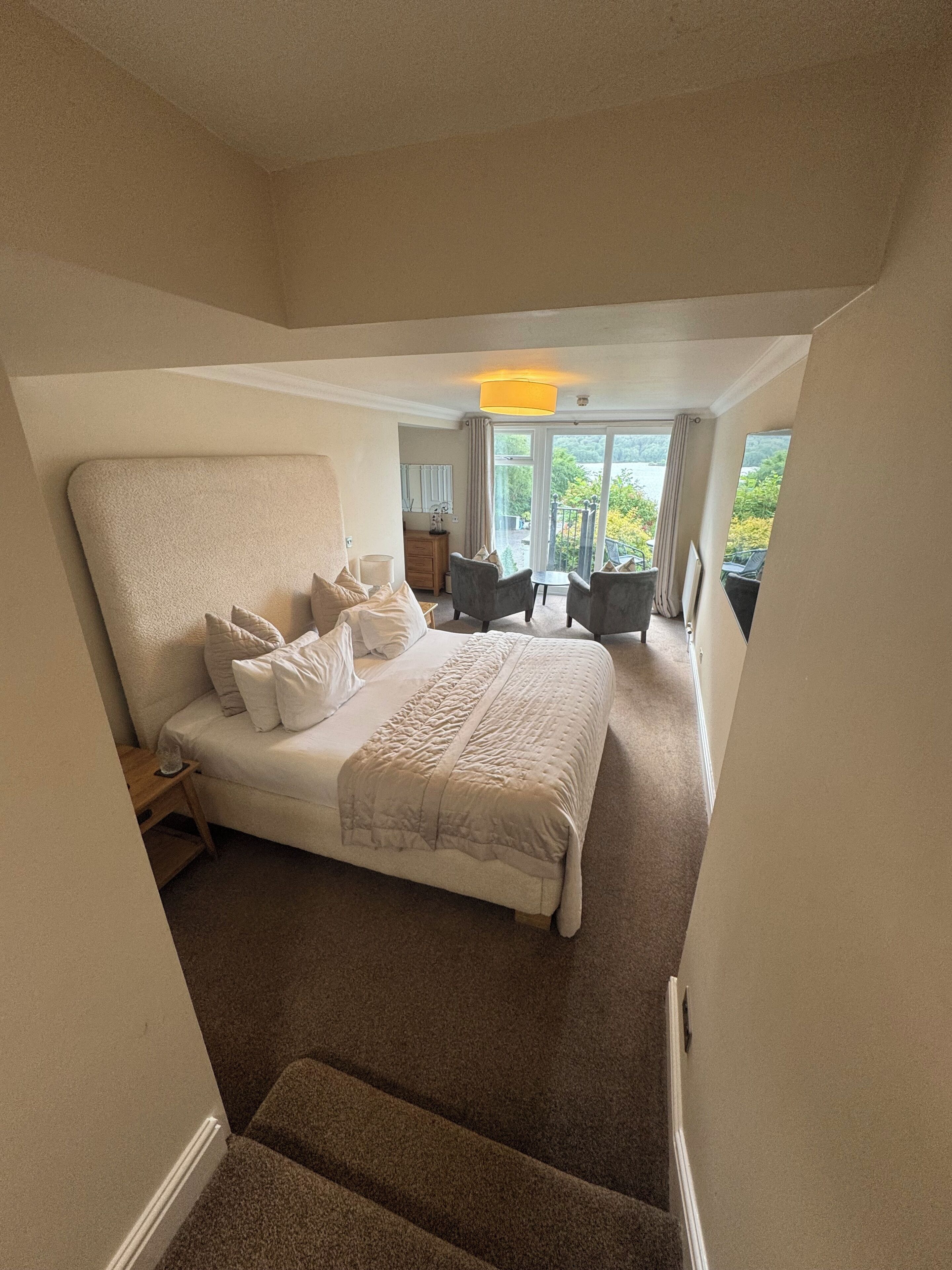 Ein Schlafzimmer mit einem großen Bett, einem kleinen Schreibtisch, einem Stuhl und Blick ins Freie.