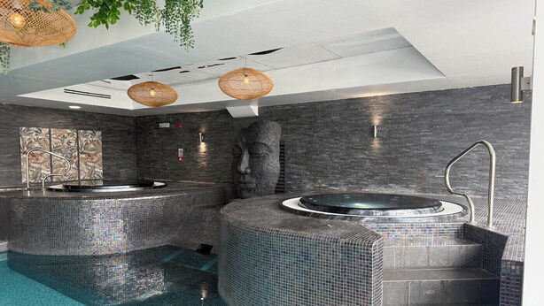 Un spa moderno con una piscina grande, dos jacuzzis y una estatua de piedra.