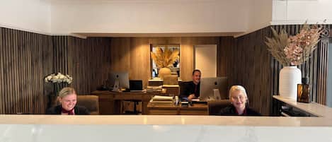Un espace de bureau moderne comprenant un comptoir d’accueil, un lambris en bois et deux personnes assises à des bureaux équipés d’ordinateurs.