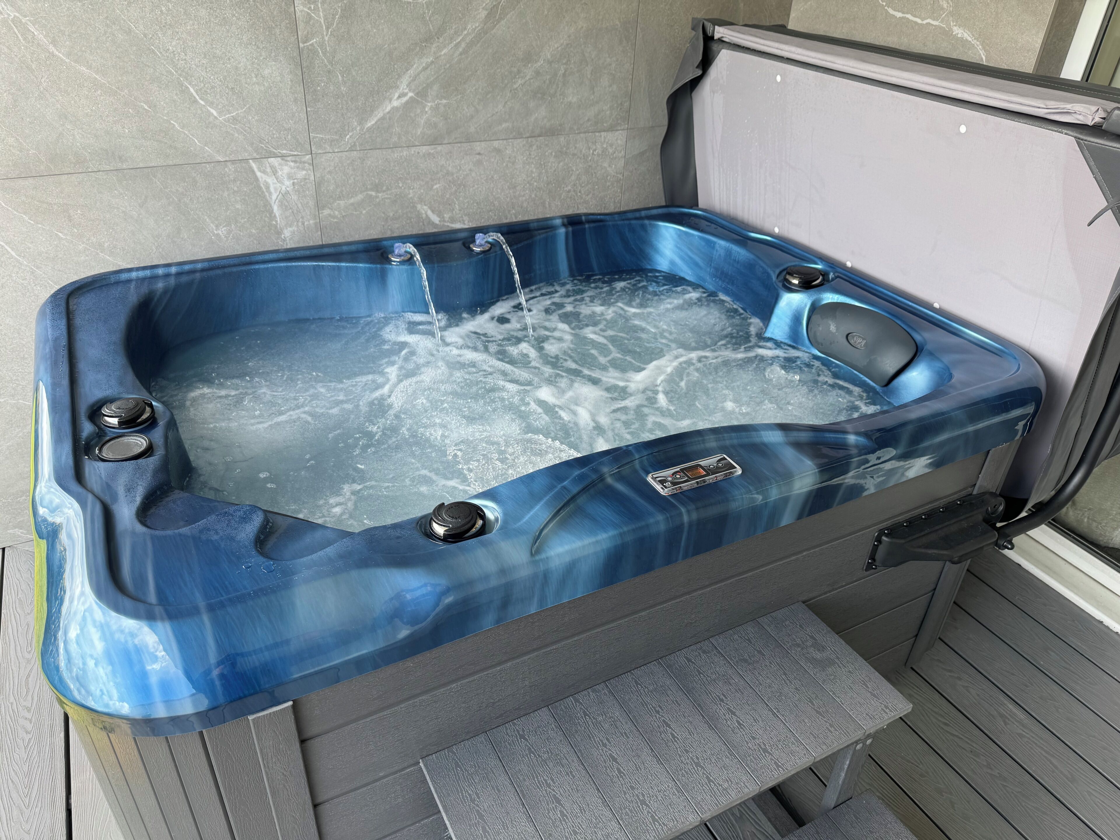 A hot tub with controls, a control panel, and a step leading into it.