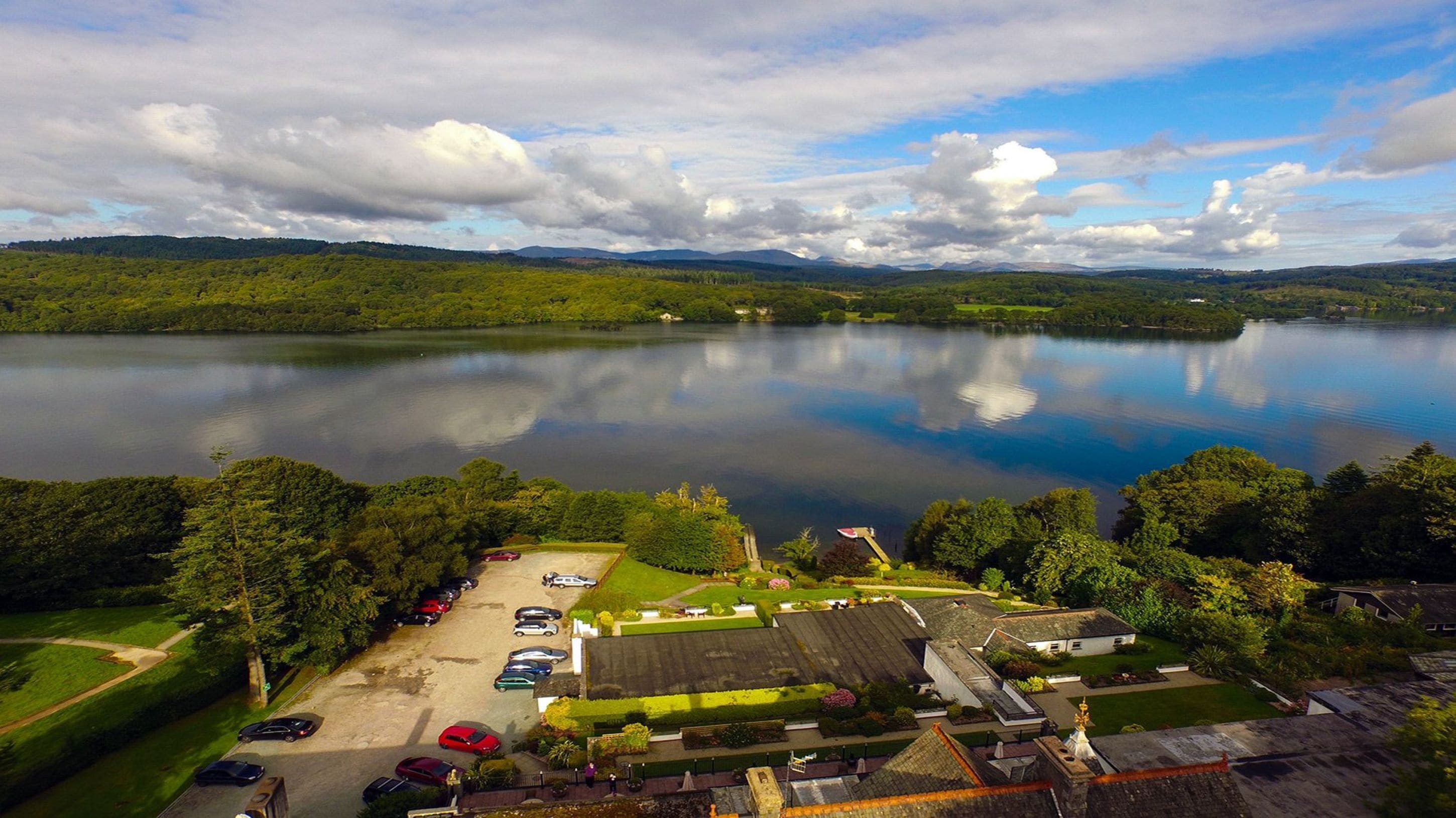 A lakeside property with a parking area, a small building, and a view of the lake and surrounding hills.