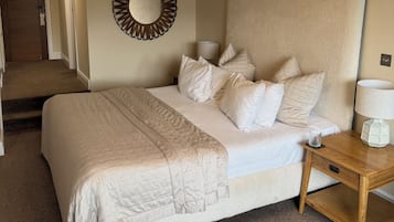 Quarto com uma cama grande, mesa de cabeceira com abajur, espelho na parede e piso coberto por carpete.