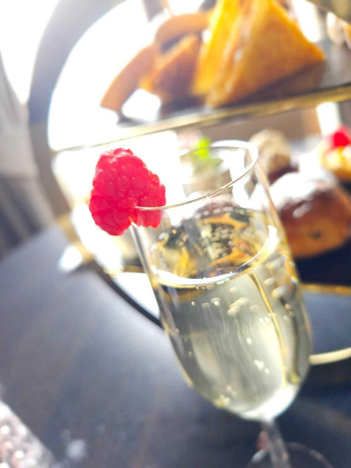 Een glas champagne met een framboos, een dessertbord met gebak, en een sandwich op de achtergrond.