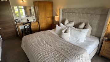 Een slaapkamer met een groot bed, een houten garderobe, een bureau met stoel en een spiegel.