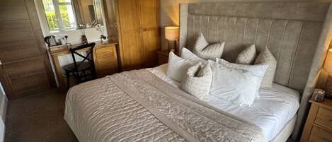 Un dormitorio con una cama grande, un armario de madera, un escritorio con una silla y un espejo.