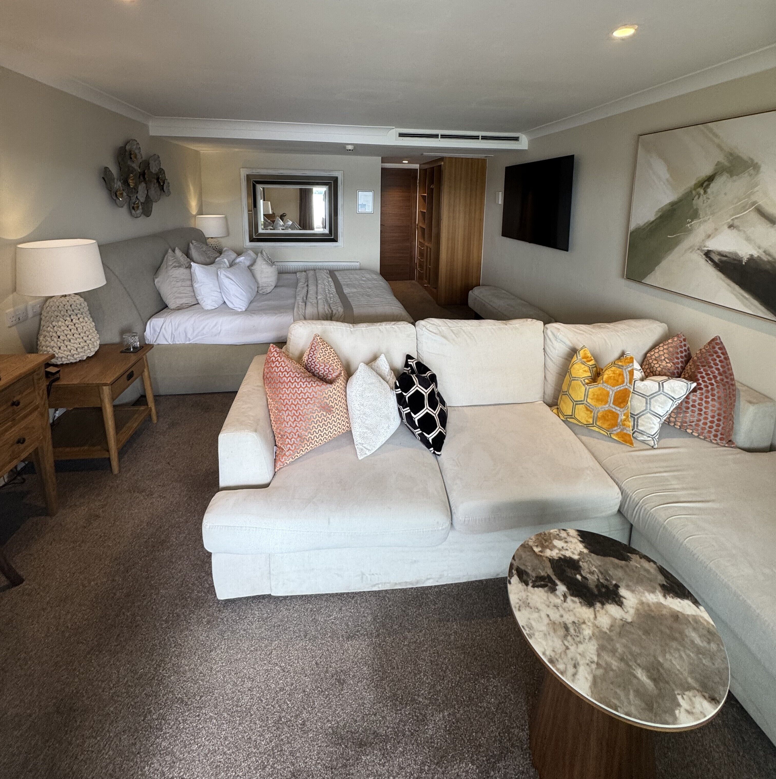 A modern living room with a large sectional sofa, a small side table, a lamp, and a painting on the wall.