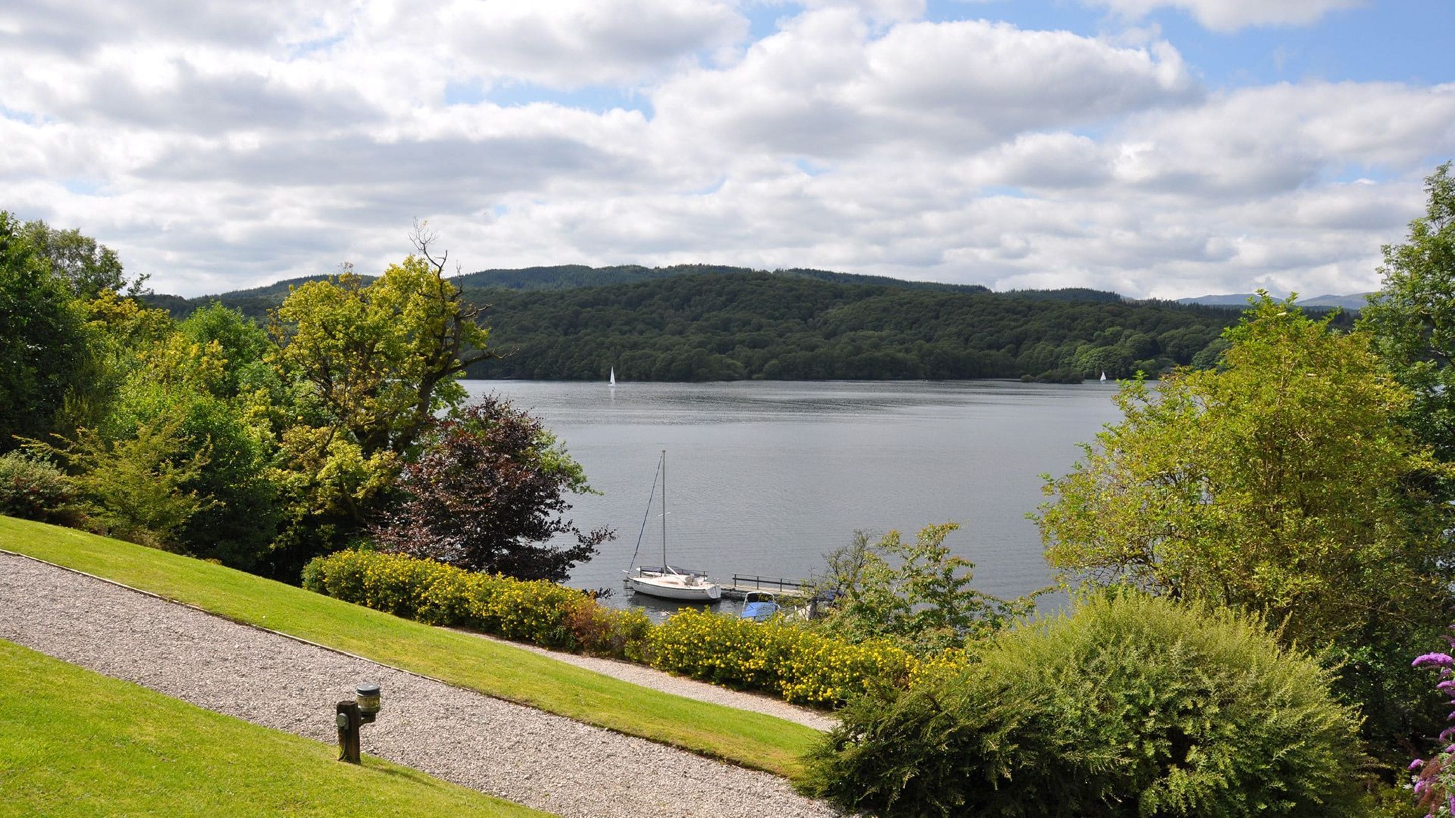 Une vue sur le lac, avec des bateaux, un sentier bordé d’herbe et une végétation luxuriante.
