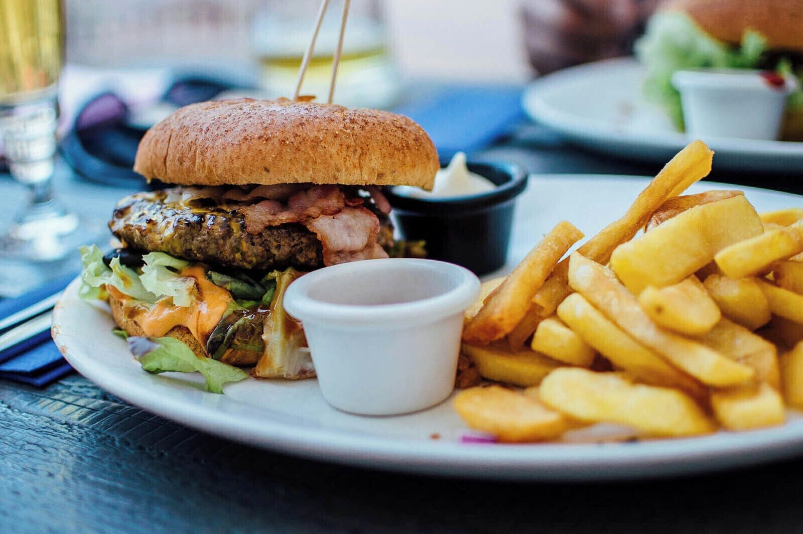 A plate with a burger, fries, and a small cup of sauce.