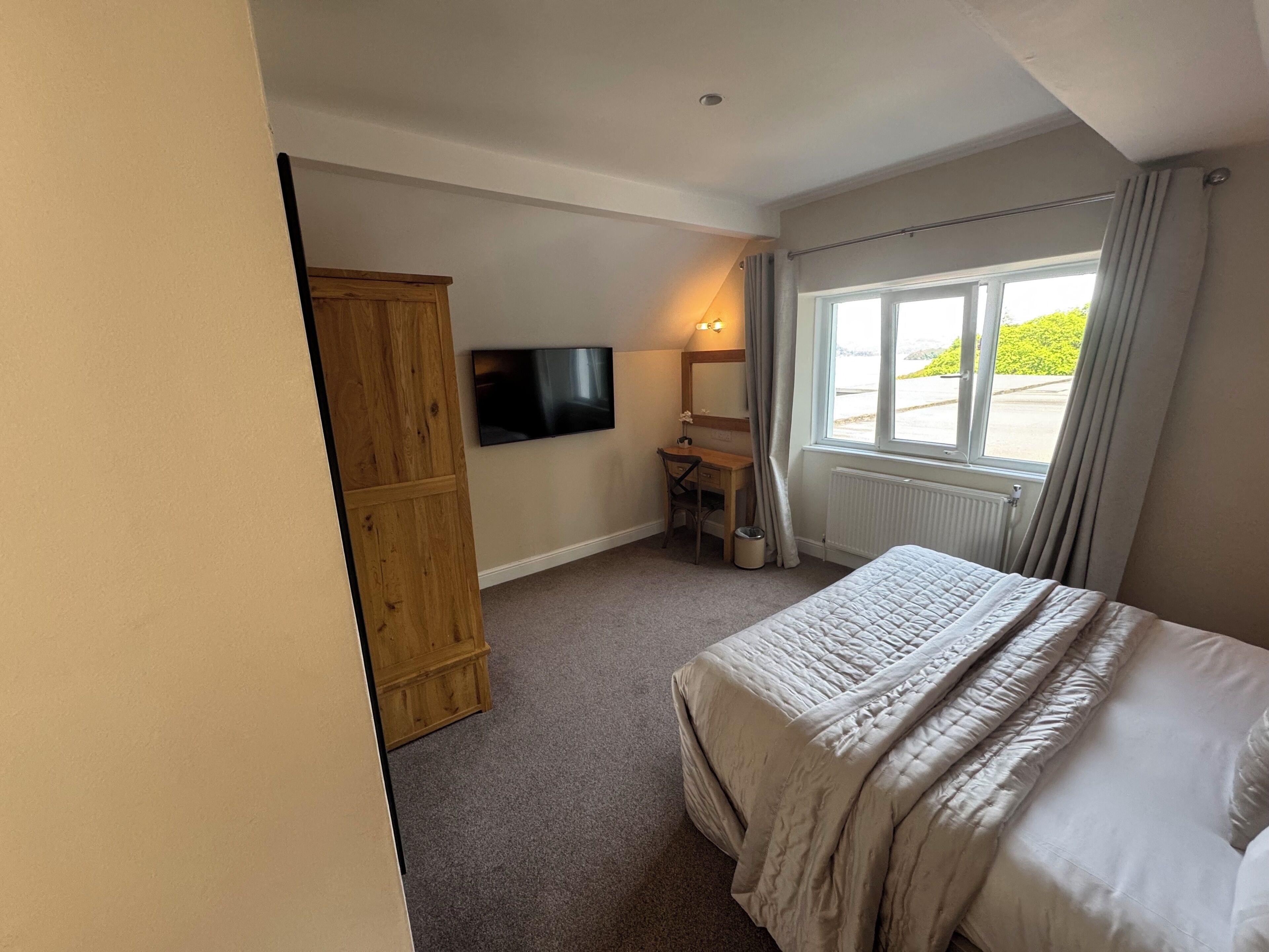 A bedroom with a bed, a desk, a television, and a window with curtains.