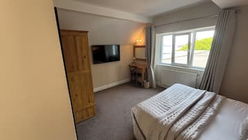Un dormitorio con cama, escritorio, televisión y ventana con cortinas.