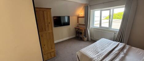 Un dormitorio con cama, escritorio, televisión y ventana con cortinas.