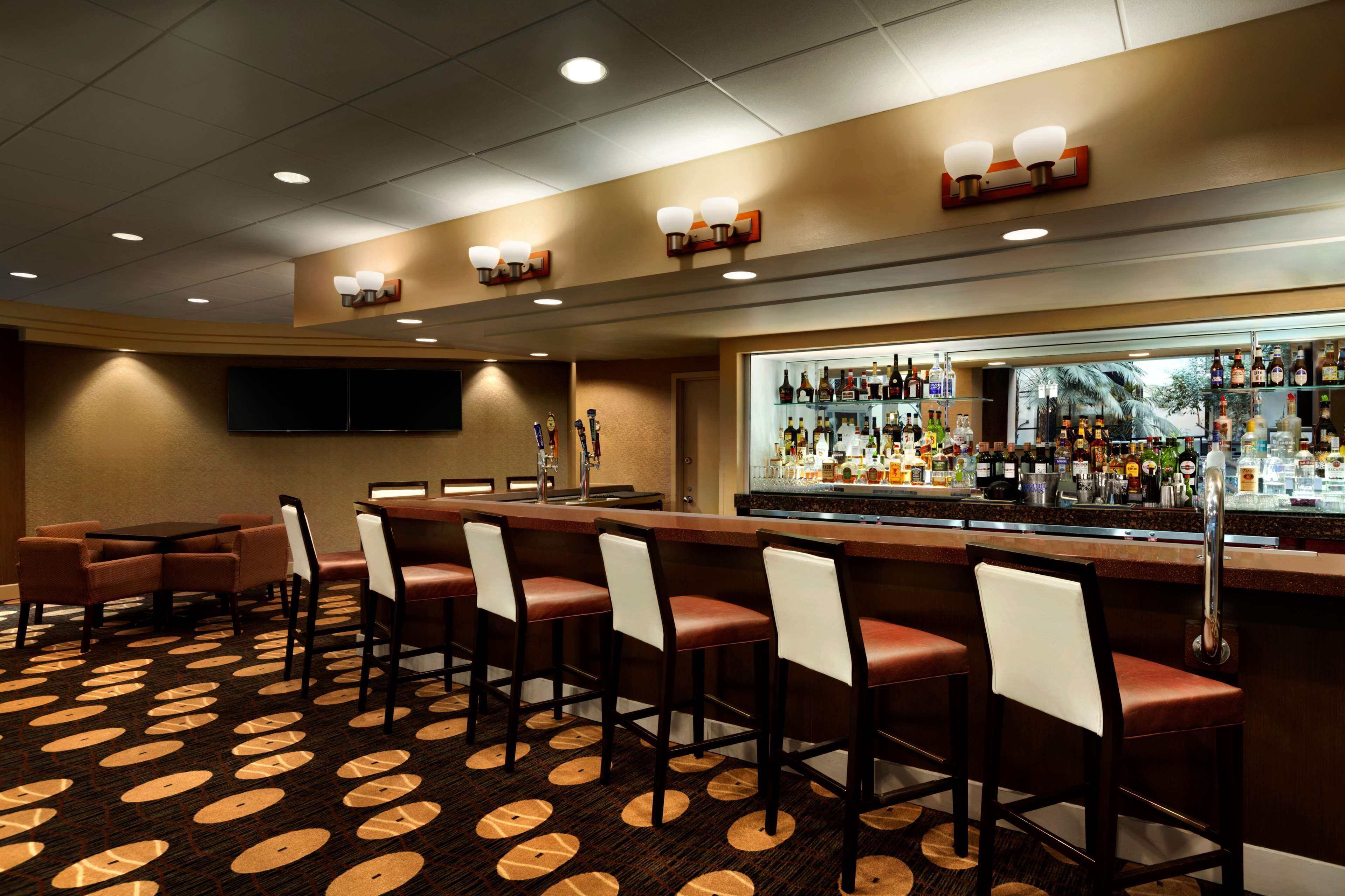 A bar area with a long counter, multiple stools, and a variety of bottles and glasses.