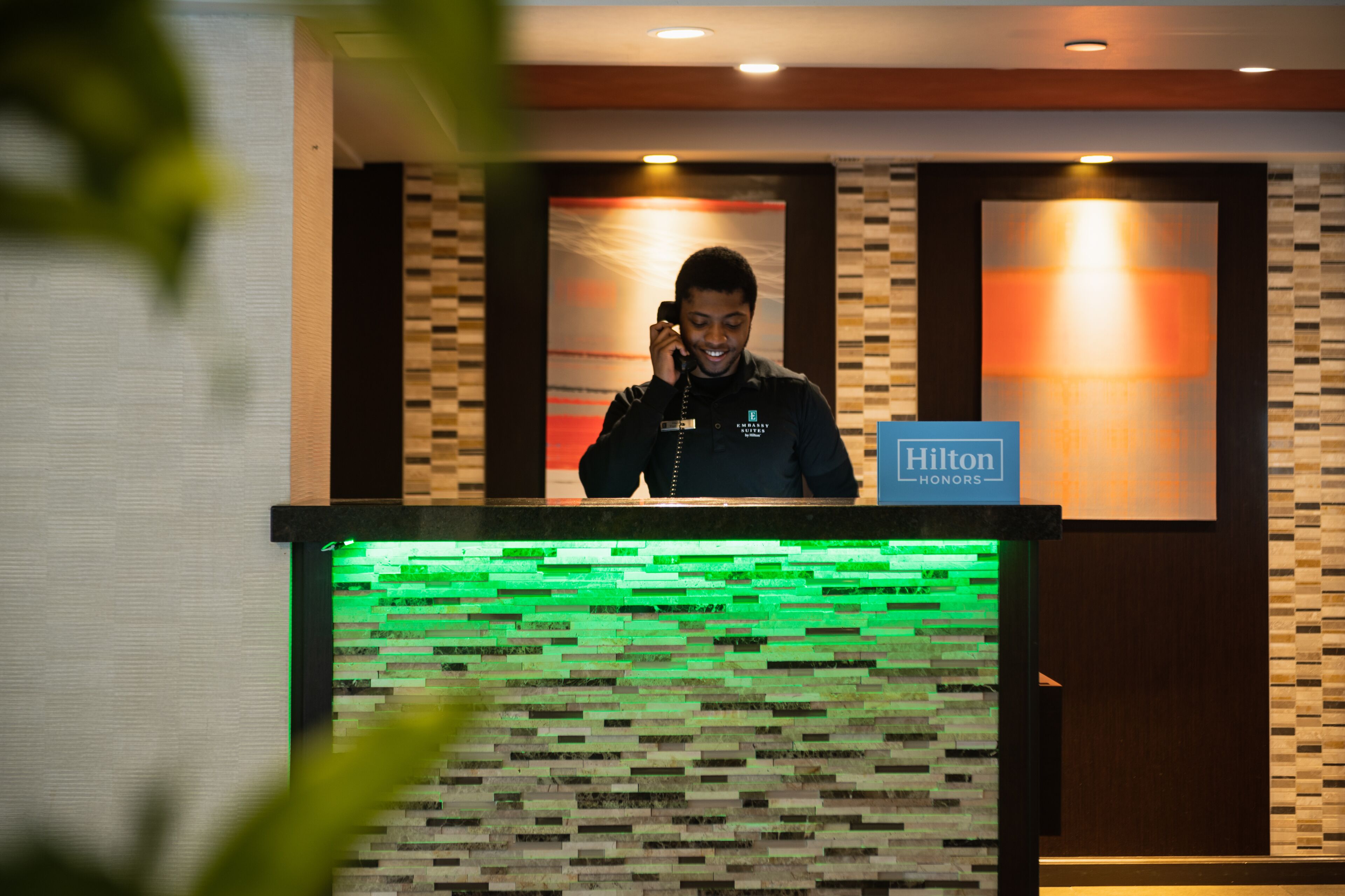 A hotel reception desk with a Hilton Honors sign, a patterned wall, and a green illuminated panel.