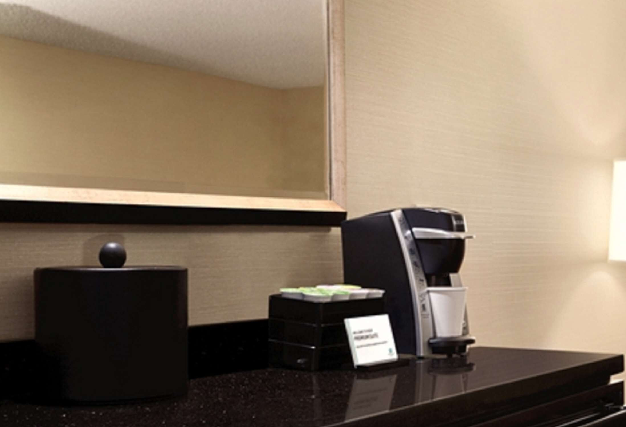 Zona de recepción de hotel con una máquina de café, un recipiente negro y una pequeña señal.