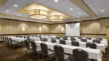 A conference room with rows of tables and chairs, a projector screen, and a carpeted floor.