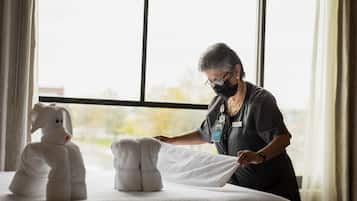 A hotel room with a bed, a window, and a person adjusting a towel.