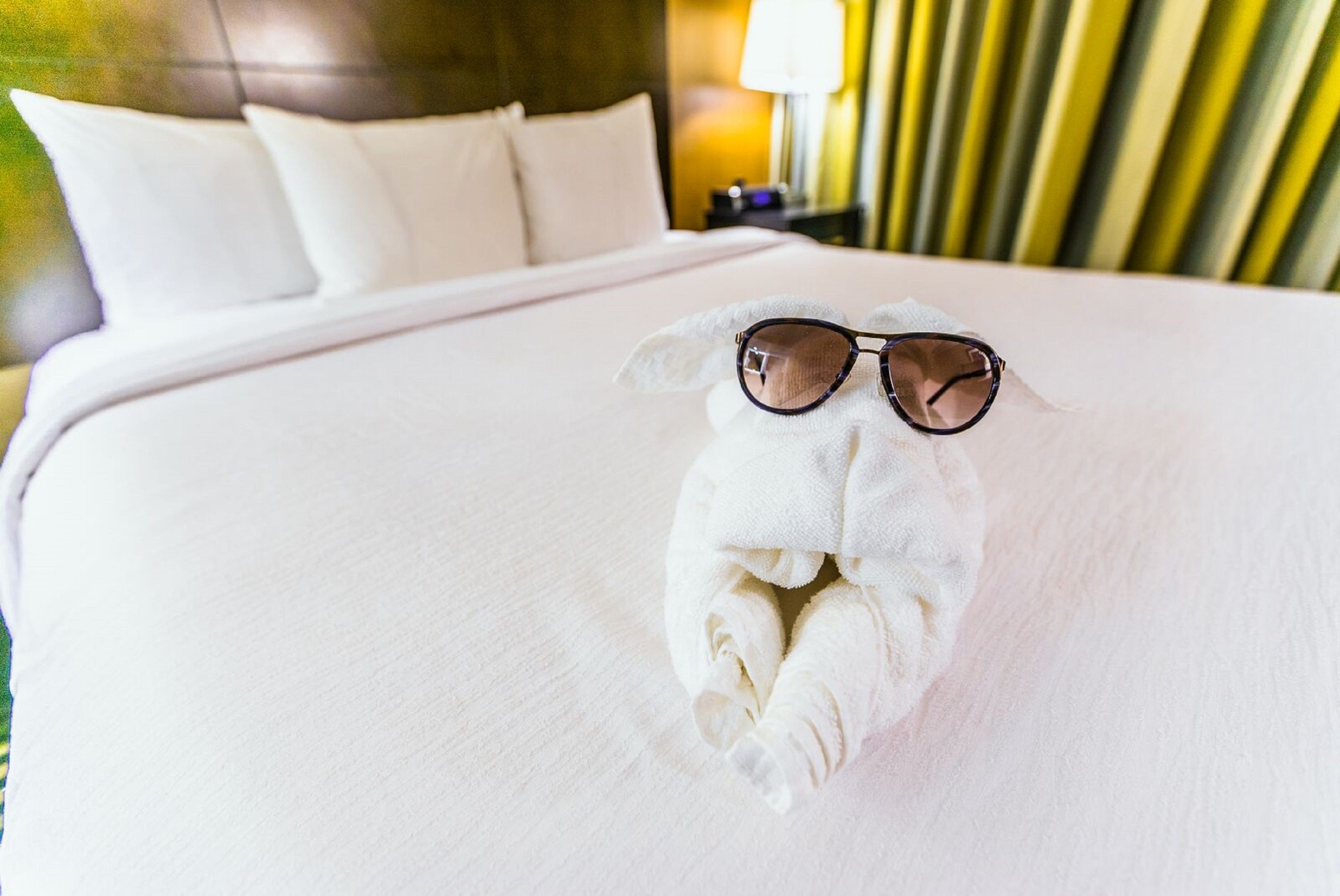 A neatly made bed with white linens and a towel folded into a shape resembling a pair of sunglasses.