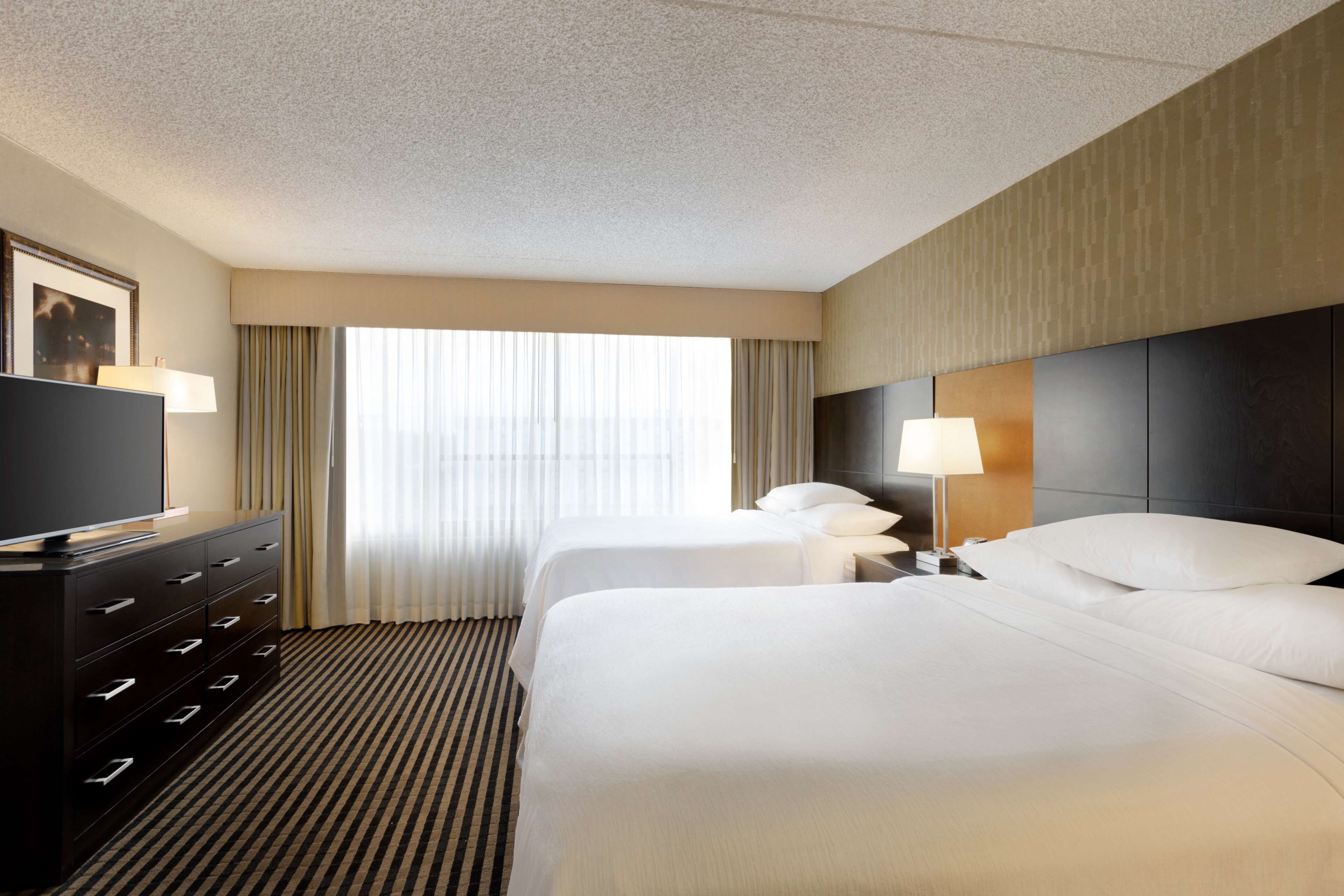 Habitación de hotel con dos camas, televisión, cómoda y ventana con cortinas.