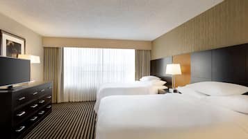Habitación de hotel con dos camas, televisión, cómoda y ventana con cortinas.