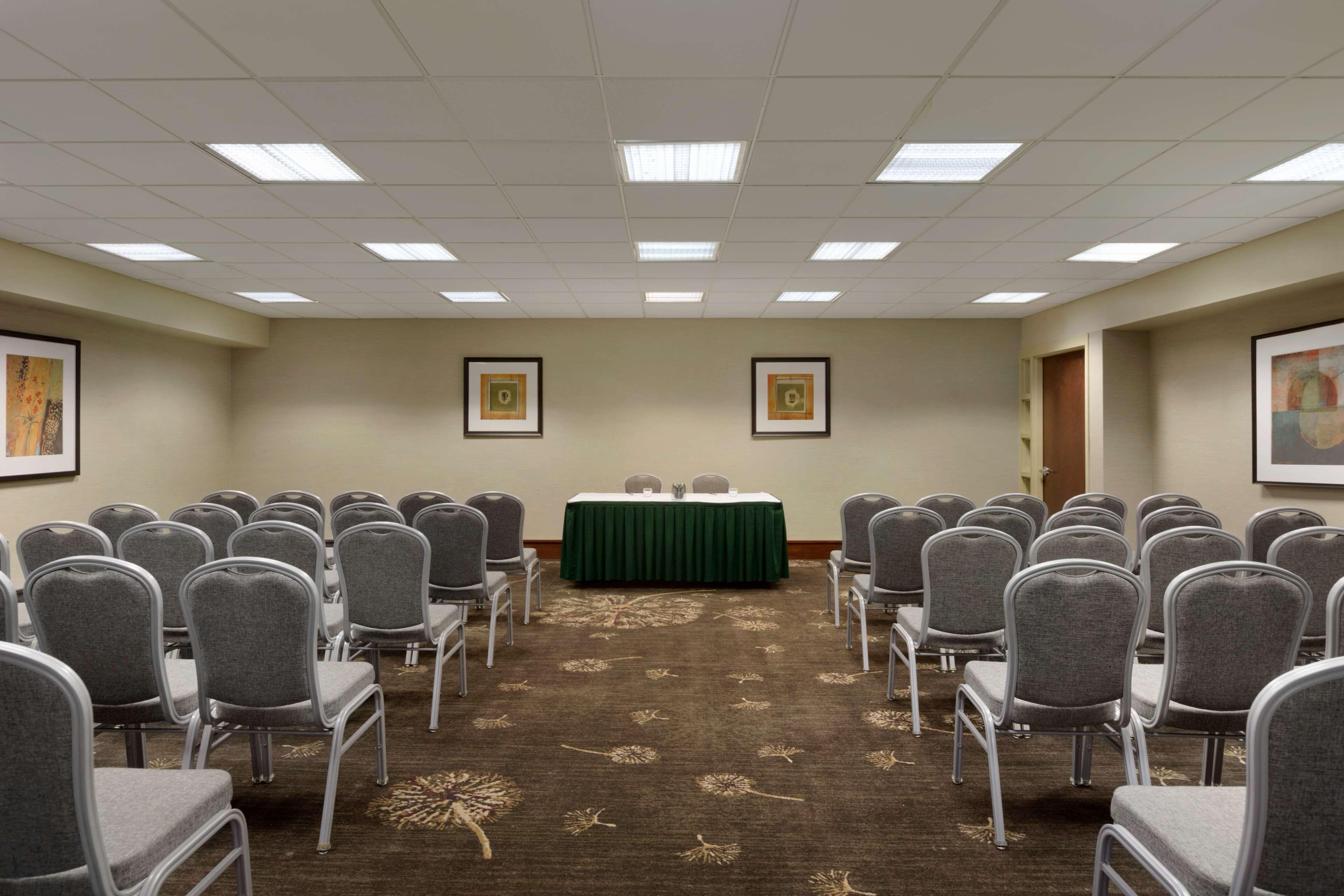 A conference room with rows of chairs facing a table, a carpet with a floral pattern, and framed pictures on the walls.