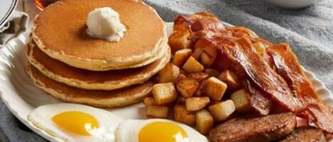 Un plato con tortitas, tocino, salchichas, huevos y patatas.