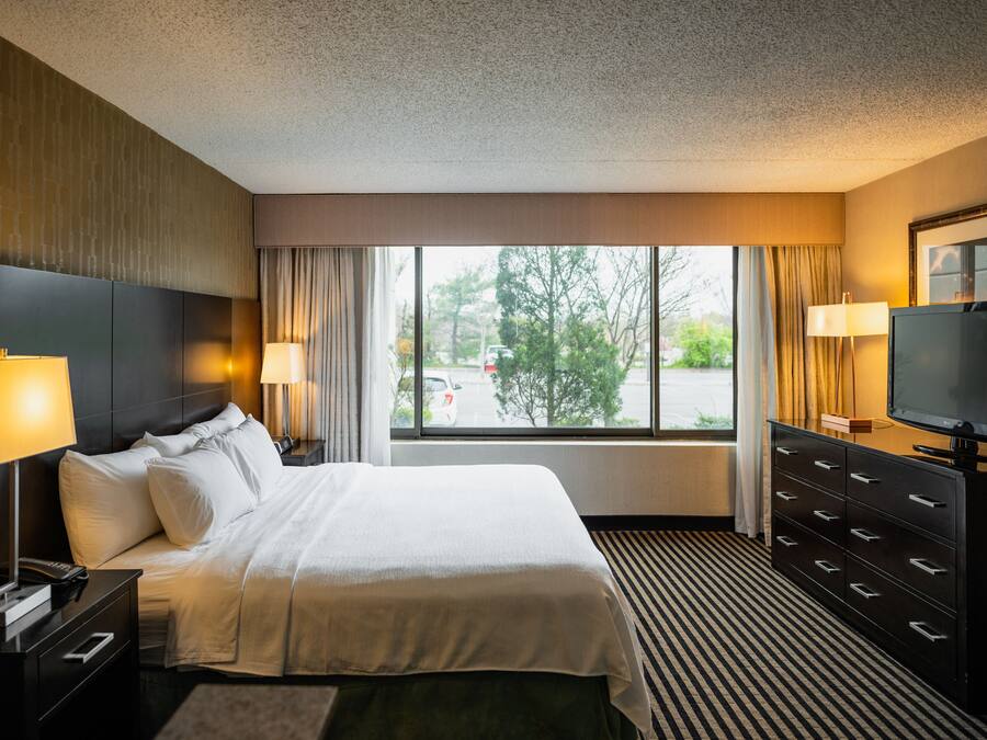 Ein Hotelzimmer mit einem großen Bett, einem Fernseher, einer Kommode und einem Fenster mit Blick nach draußen.