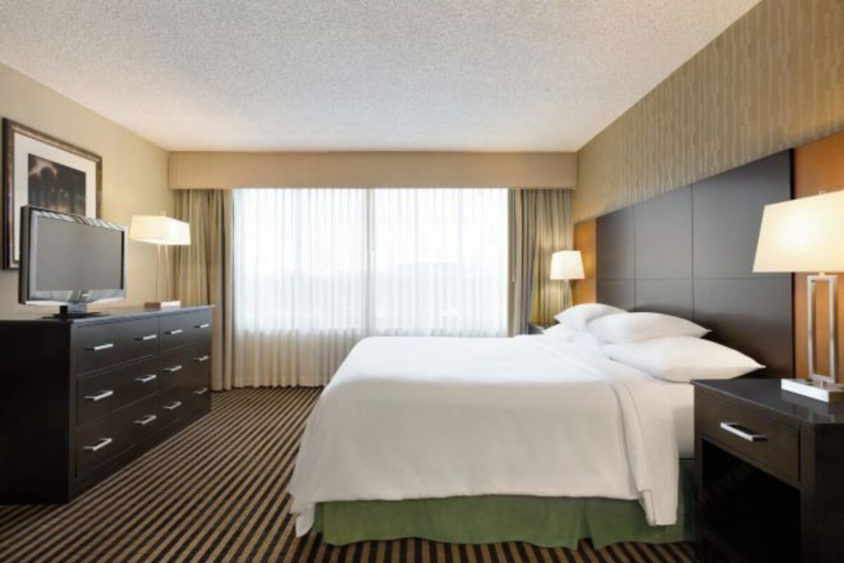 A hotel room with a bed, a dresser, a television, and a window with curtains.
